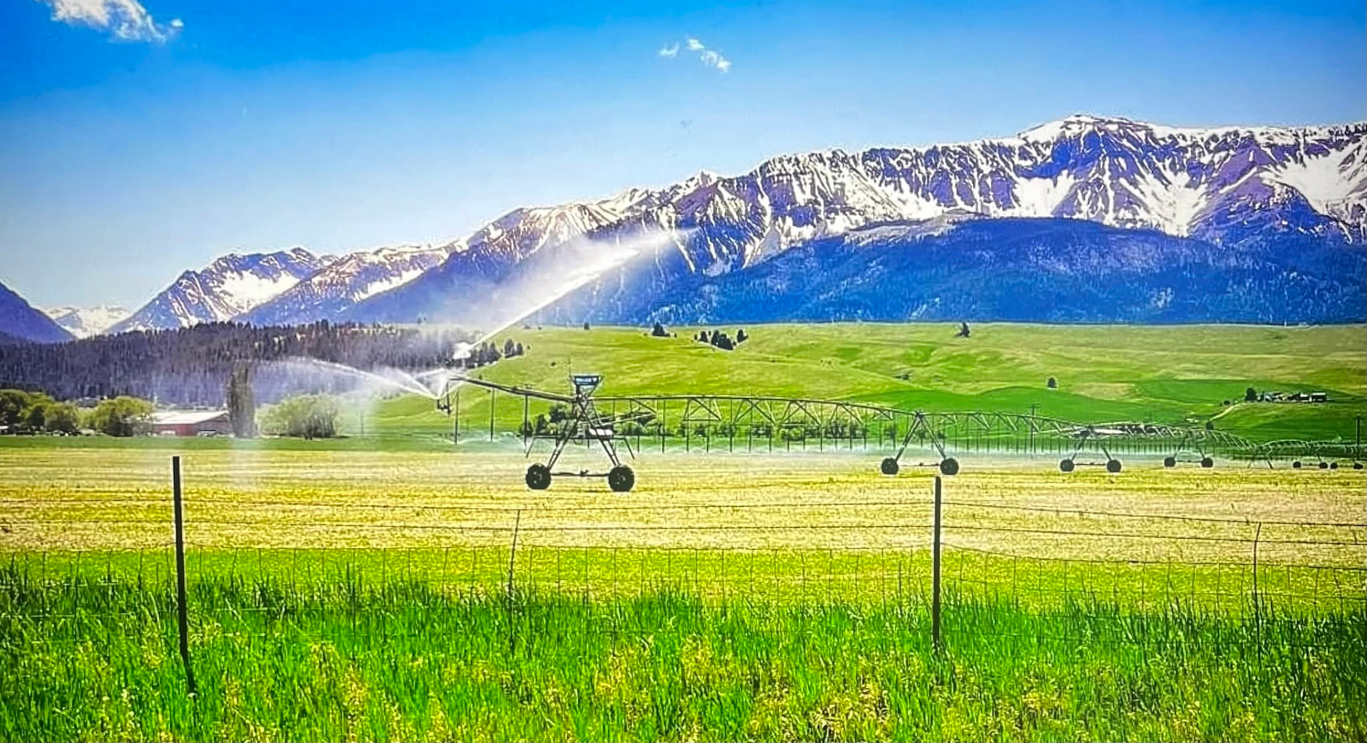 Center-pivot irrigation system spraying water across a field with snow-capped mountains in the background
