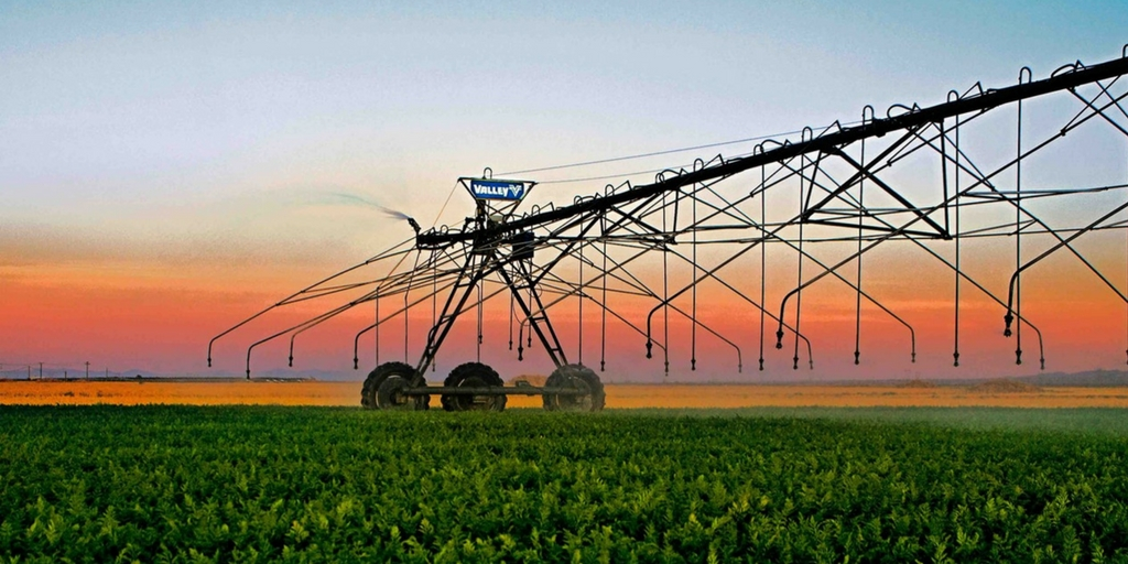 Valley center pivot standing in a green field against a colorful sunset sky